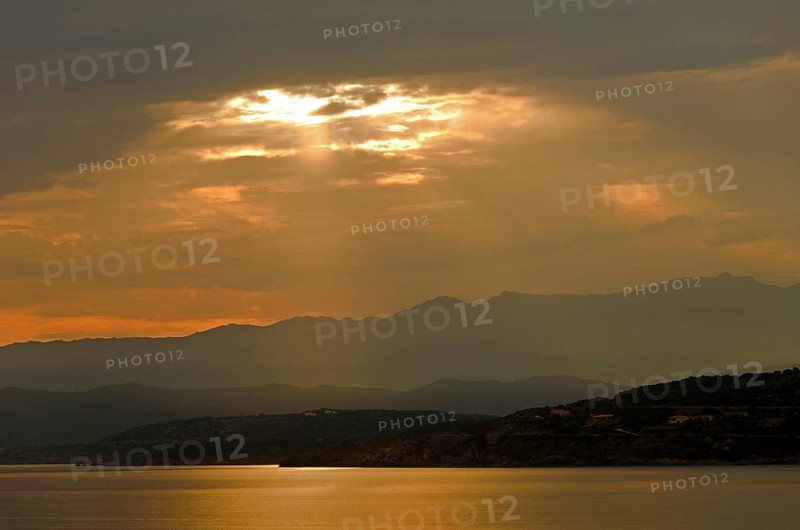 The rising sun forms sun beams behind the rocks of the island Ile de la Pietra near L'Île-Rousse. L'Île-Rousse  is in the department Haute-Corse