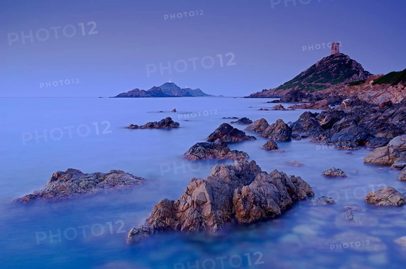The genoese tower Tour de la Parata at the right and the islands Les Iles Sanguinaires behind the rocky mediterranean coast at the blue hour before sunrise. Les Iles Sanguinaires are in the department Corse-du-Sud