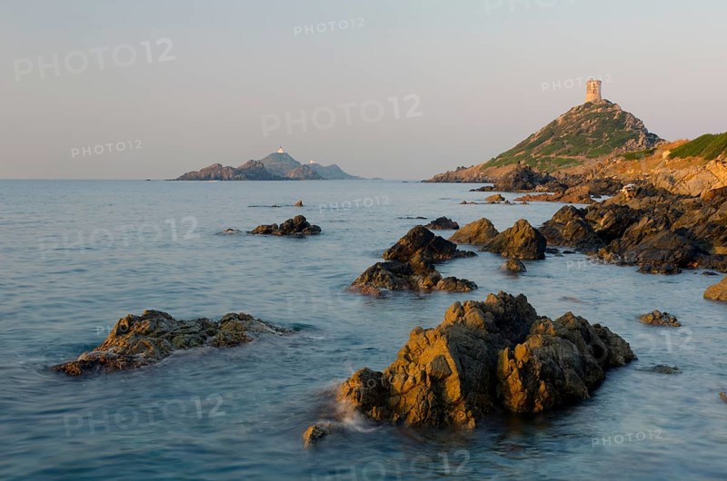 The genoese tower Tour de la Parata at the right and the islands Les Iles Sanguinaires behind the rocky mediterranean coast illuminated by warm morning light. Les Iles Sanguinaires are in the department Corse-du-Sud
