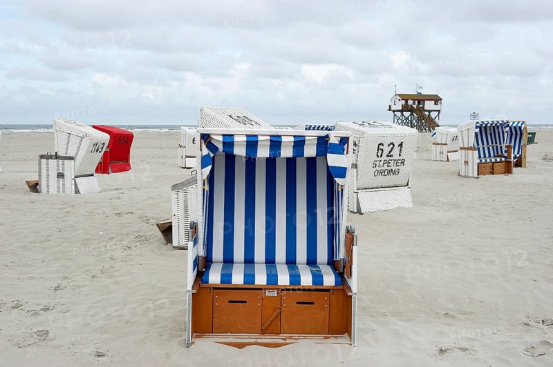Roofed wicker beach chairs on the beach in front of a house on stilts
