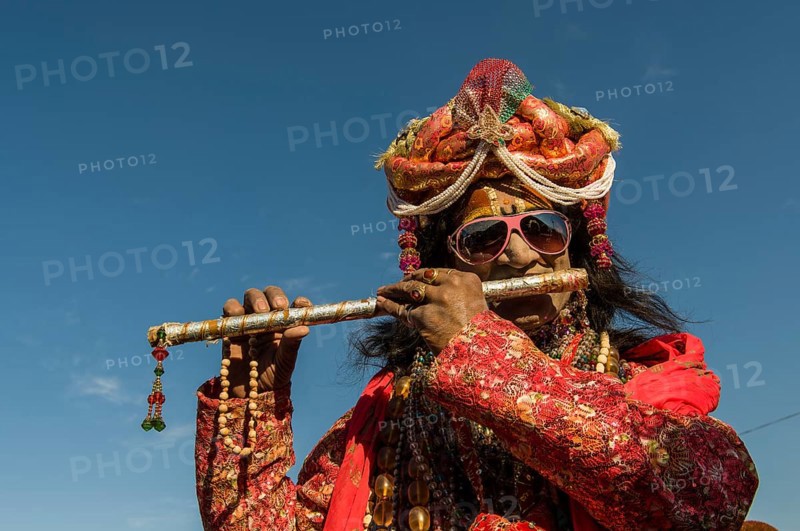 Colourfully costumed devotee playing flute during Kumbh Mela