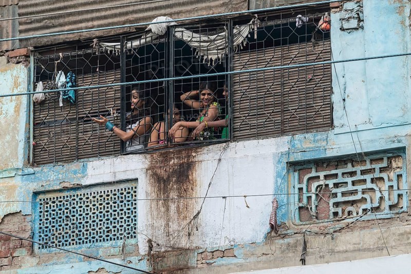 Prostitutes looking out of a window secured with bars waving to potential customers in the redlight district
