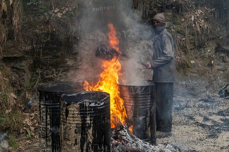 A worker heating tar in barrels with an open fire at a road construction site