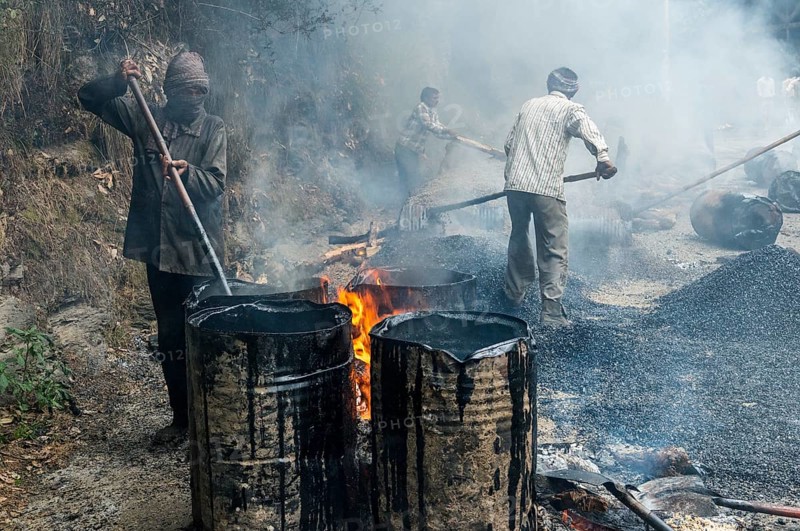 A worker heating tar in barrels with an open fire at a road construction site