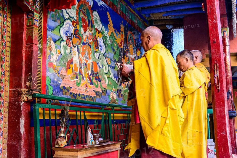Three monks of Lamayuru Gompa are praying in front of a colorful religious wall painting