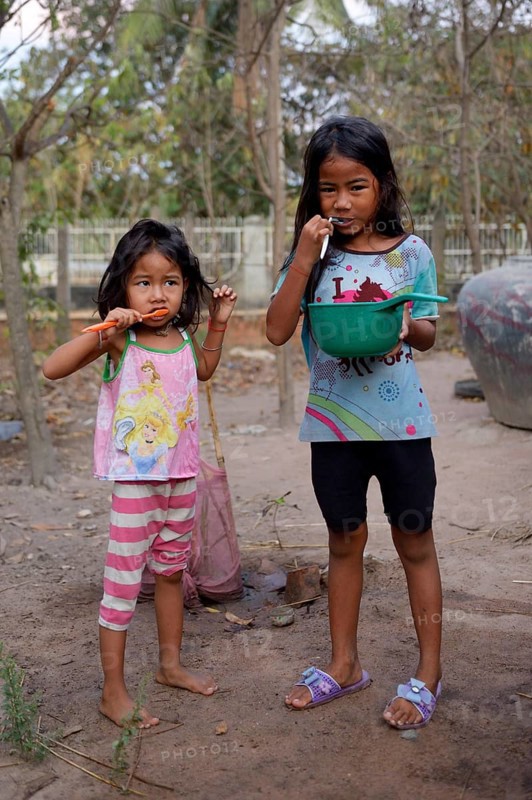 Two girls brushing their teeth outside a house