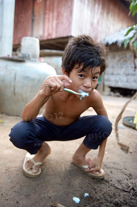 Young boy brushing his teeth outside a house