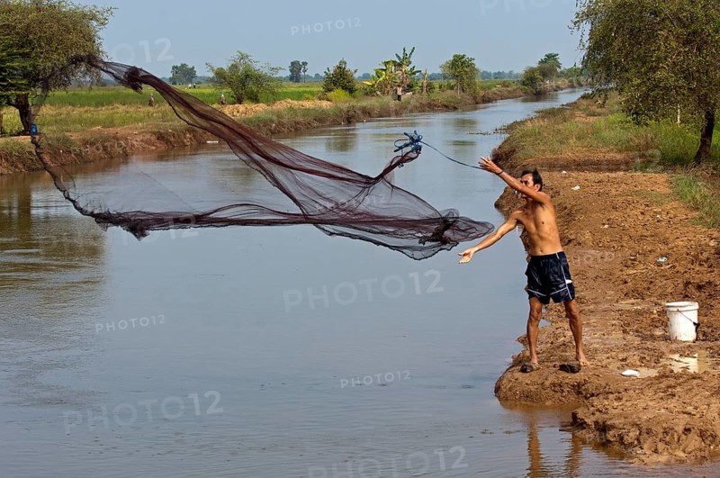 Fisherman fishing by casting a throw net in a river