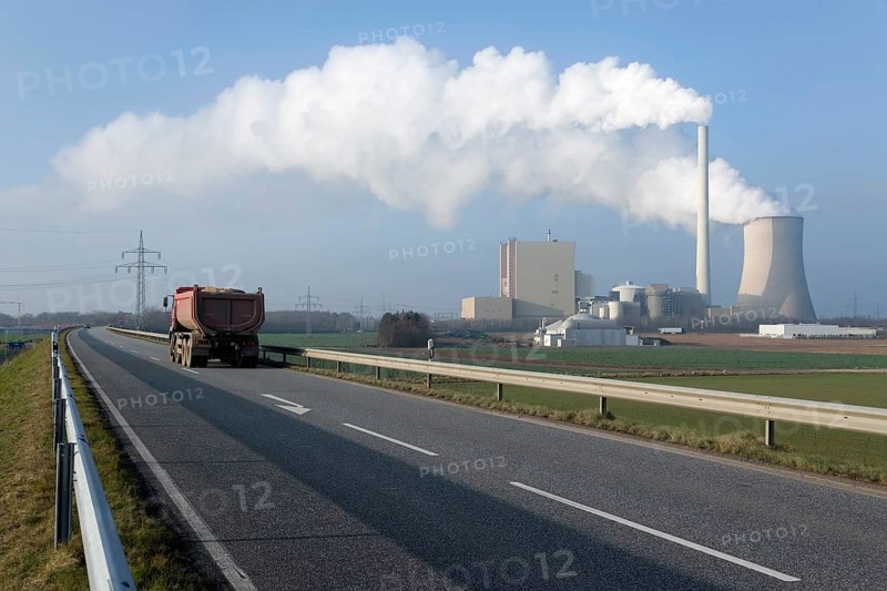 Lorry on a two-lane highway travelling in front of steam rising from a cooling tower and a chimney of Petershagen-Lahde coal-fired power station