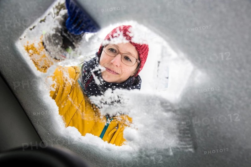 Young woman cleaning a car of ice and snow