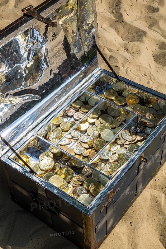 Treasure chest with gold and silver coins on the sand