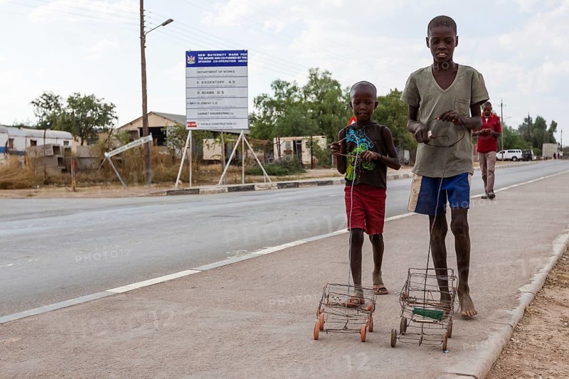 Two Himba boys playing with their self-made toy cars by the roadside