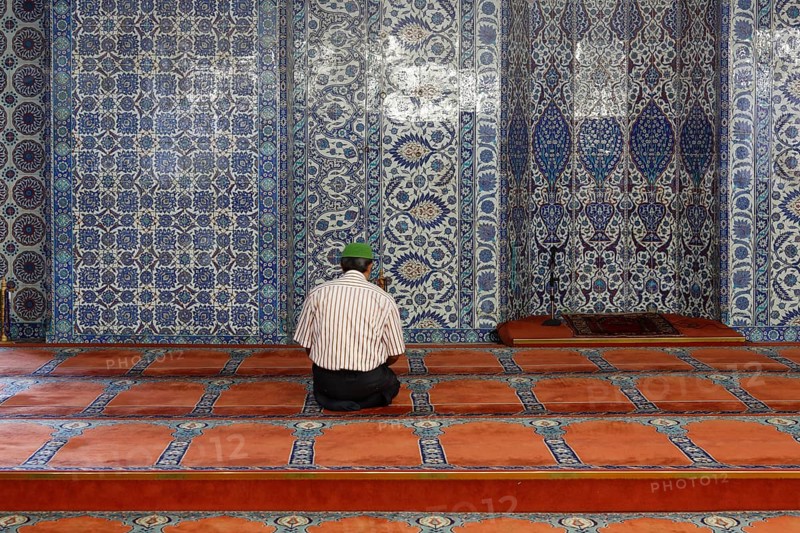 Man in prayer in front of a wall with Iznik faience tiles