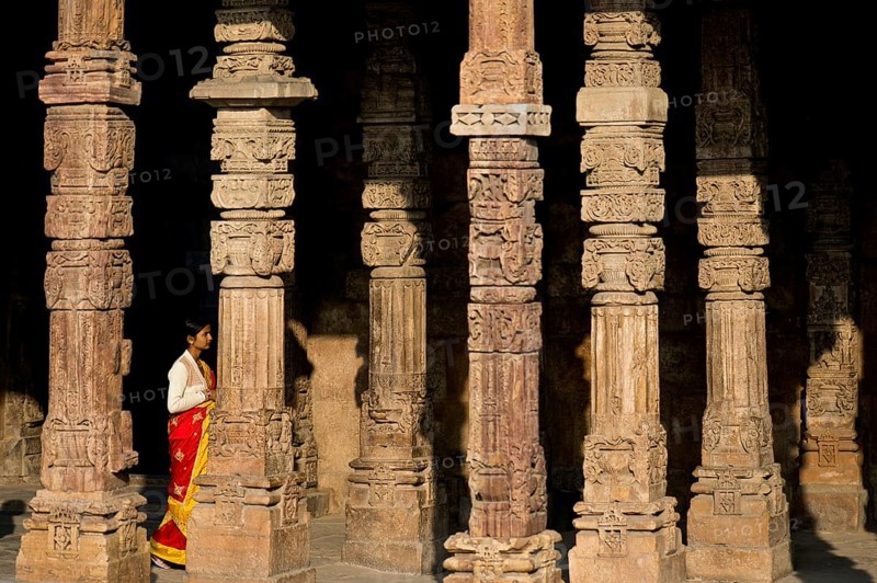 Indian woman walking in between ornately carved stone pillars