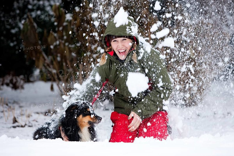 Young woman playing with an Australian Shepherd dog in the snow