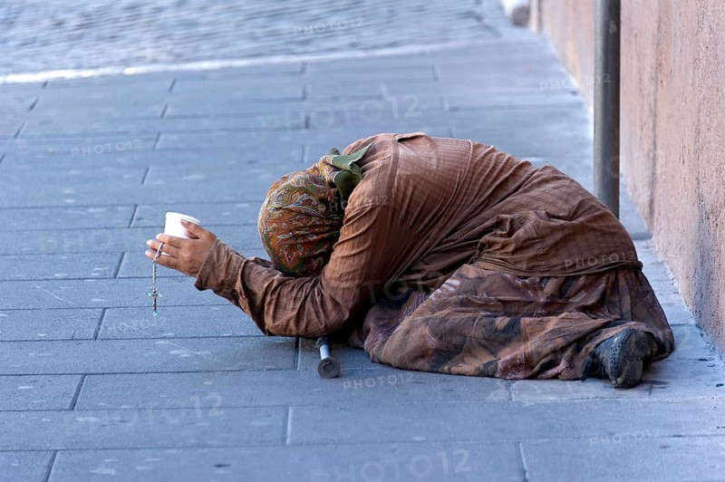 Female beggar holding a plastic cup in a street of the old town
