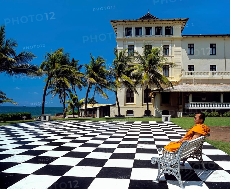 Monk sitting on a bench on a mosaic terrace in the garden in front of the Galle Face Hotel