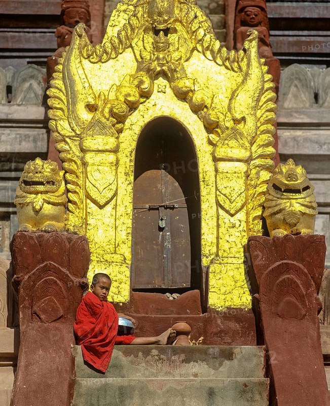 Monk sitting on a staircase at the door of Shwezigon Pagoda with its golden chedi