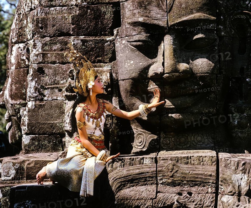 Temple dancer or apsara sitting in front of a face tower at Bayon Temple