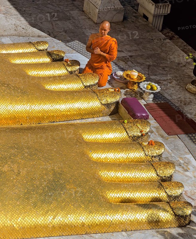 Monk praying at the feet of the golden Buddha statue of Wat Intharawihan