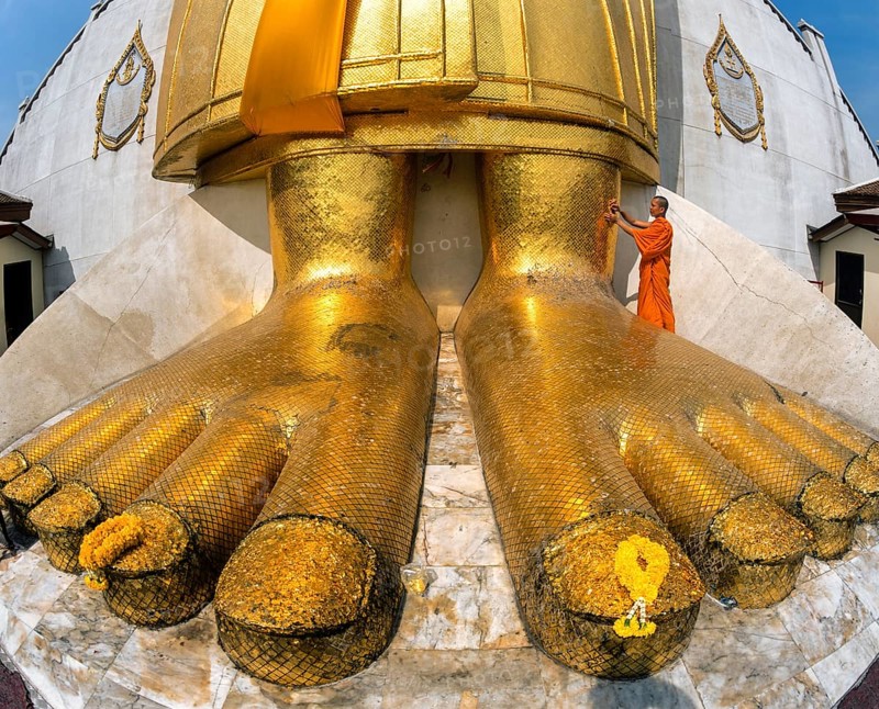 Monk praying at the feet of the golden Buddha statue of Wat Intharawihan