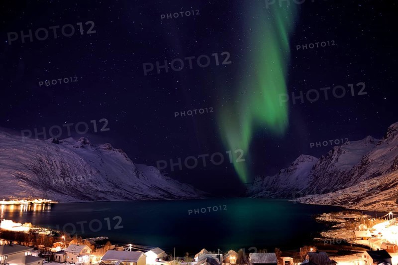 Aurora over a fjord with snow-covered mountains and an illuminated village