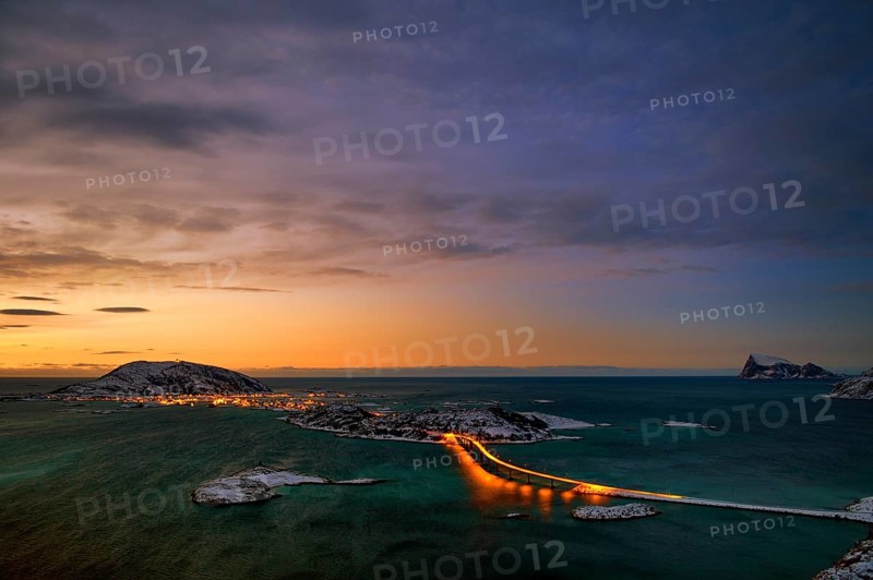 Fjord with an illuminated bridge in winter at sunset