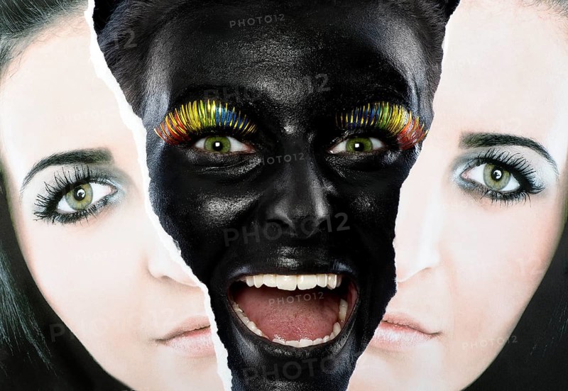 Face of a laughing young woman painted with black facepaint looking through a torn portrait photo