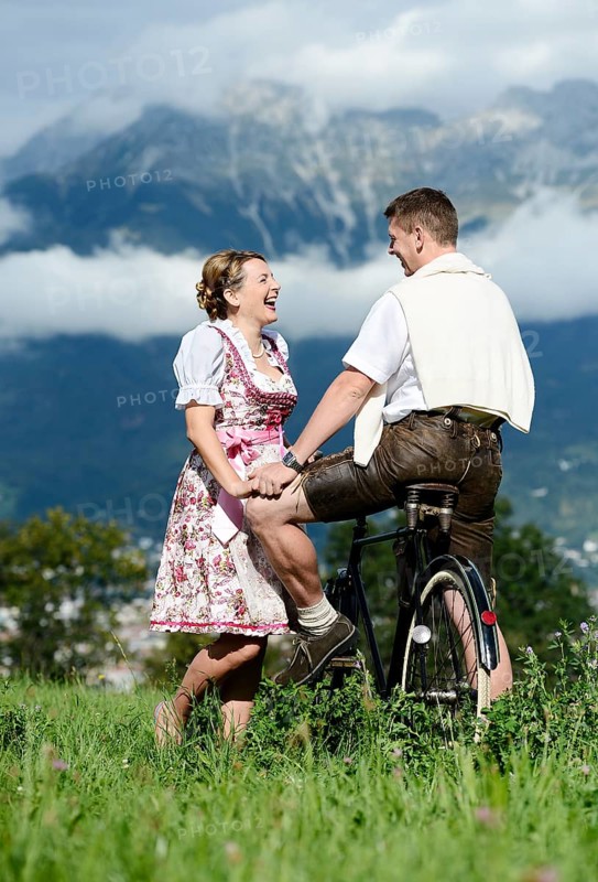 Man and a woman wearing traditional costume with an old bicycle within a natural landscape