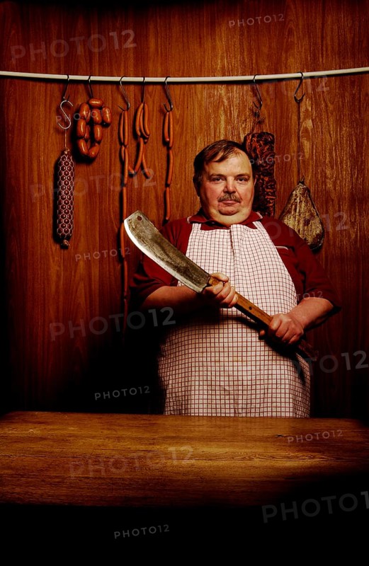 Fat butcher holding a meat cleaver in a butcher's store with a wooden ambience