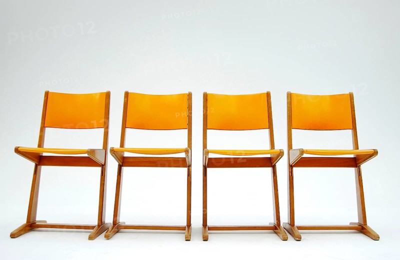 Four old orange school chairs standing side by side