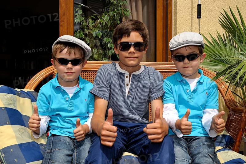 Twins and their older brother sitting together on a bench on a terrace