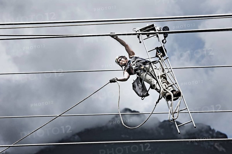 High-voltage service technician pulling a rope to get to the next pylon