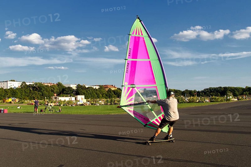 Windskater practicing on the asphalt runway with a windsurfer sail and a longboard