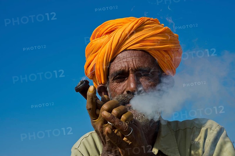 Elderly Rajasthani man with an orange turban smoking a hash pipe or hooka