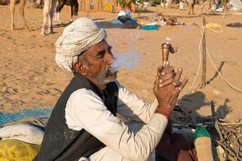 Indian with a turban sitting on the ground smoking a hash pipe