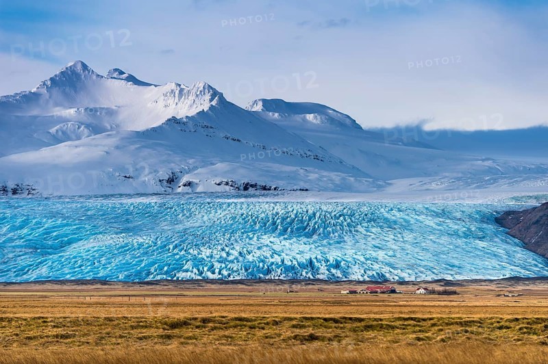 Icelandic farmstead with glacier tongue and snow-covered mountains