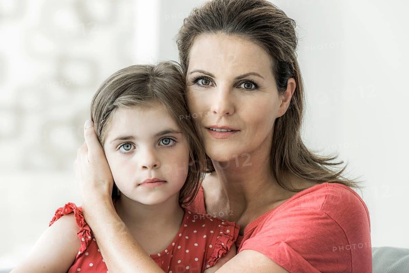 Mother and daughter sit together on the couch and look into the camera