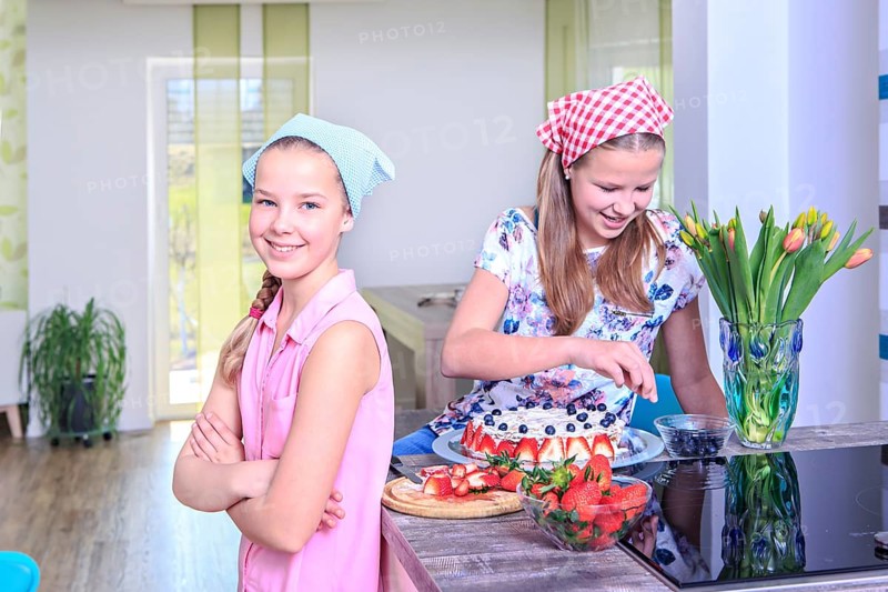 Teenage girls baking a cake at home with fresh fruit