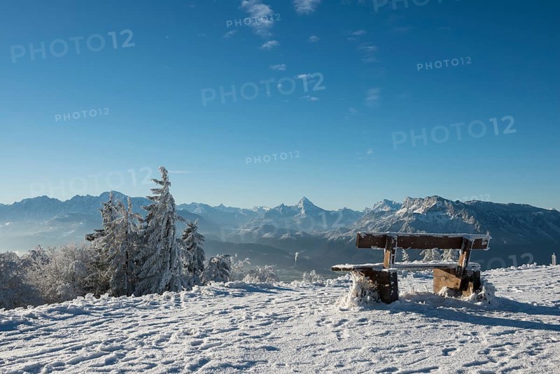 Snow-covered bench in front of Alpine panorama