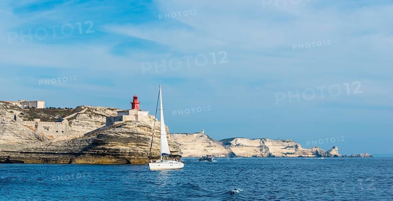 Sailing boat off the chalk cliffs and the lighthouse of Bonifacio