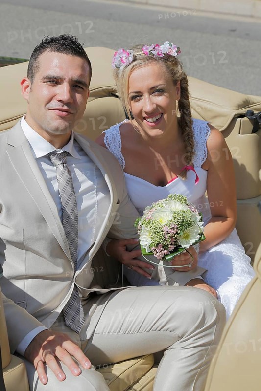 Bride and groom posing in the back seat of an open car