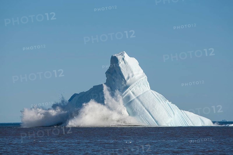 Pieces breaking off an enormous iceberg causing it to unbalance and collapse