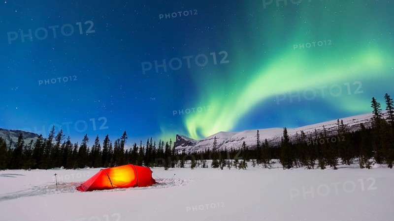 Northern Lights (Aurora borealis) above a red illuminated tent in winter