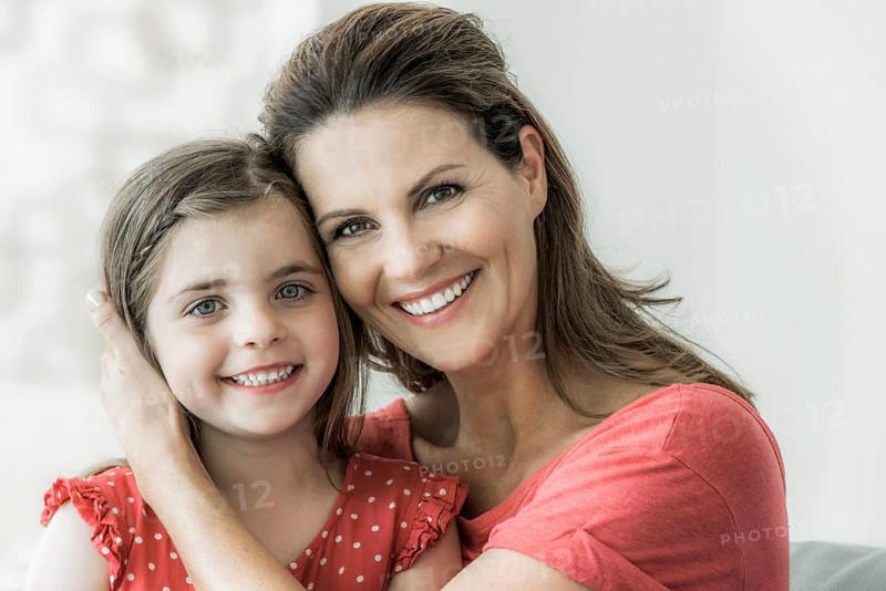 Mother and daughter sit together on the couch and look into the camera