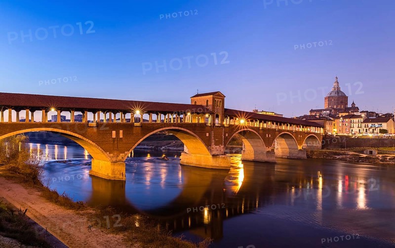 Illuminated bridge Ponte Coperto leads over the river Ticino with cathedral
