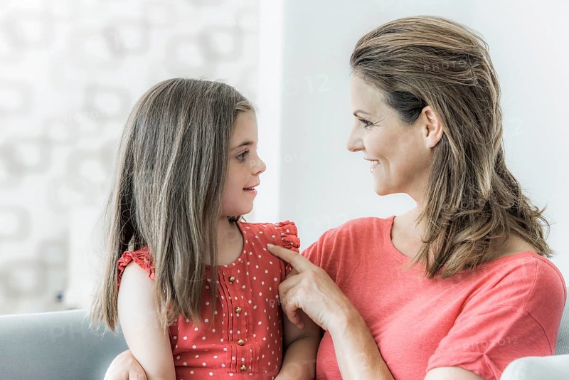 Mother and daughter sit together on the couch and look at each other