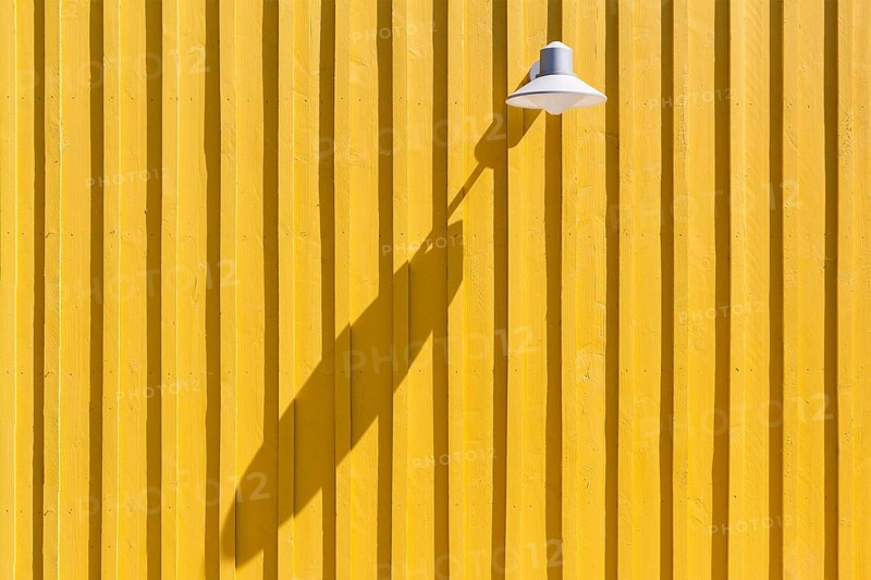 Lamp on a yellow beach hut casting a long shadow