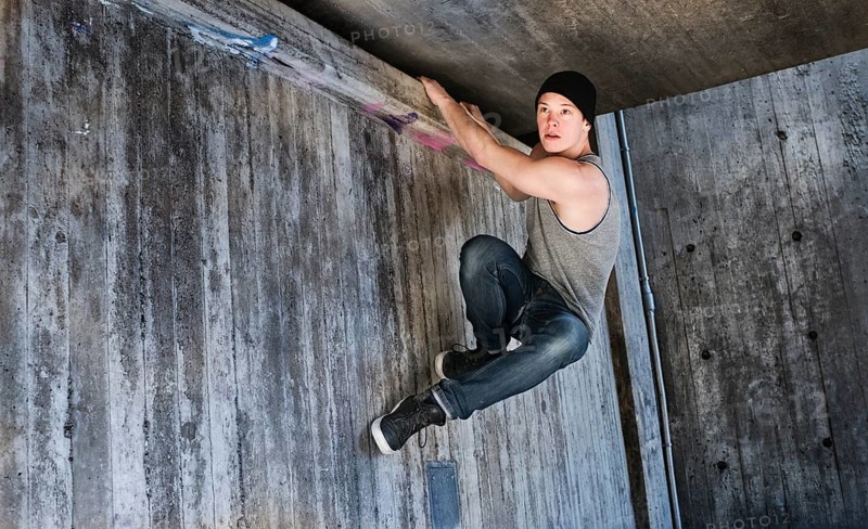 Young man hanging in a parkour move on concrete wall