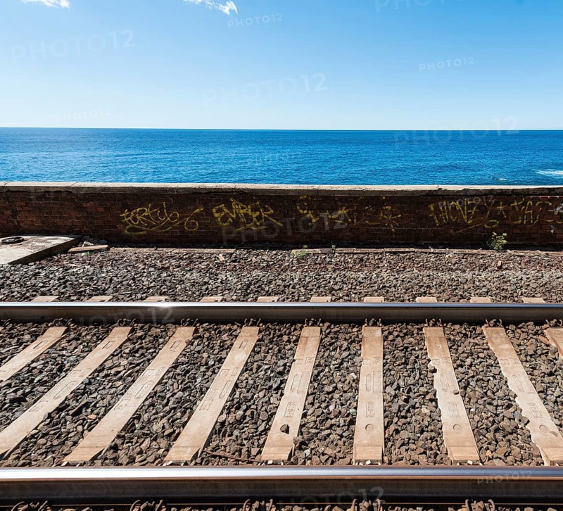 Railroad tracks in front wall with graffiti in front of the sea